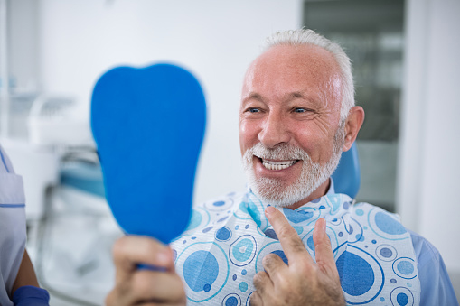 Older man looking at teeth in hand held mirror
