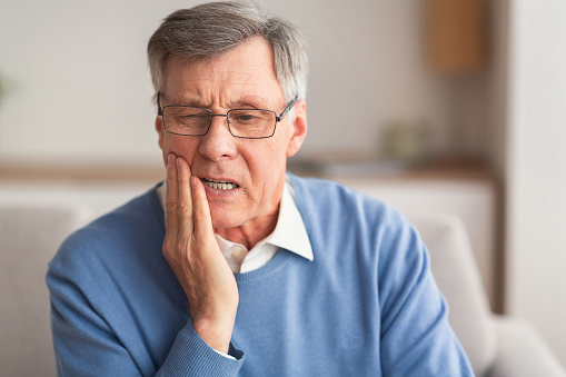 Older man holding his jaw in pain.