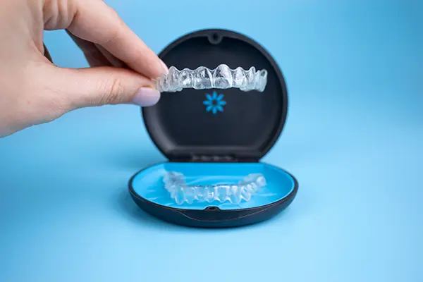 A hand picking up the upper tray of an Invisalign clear aligner set, showcasing its transparency and light weight.